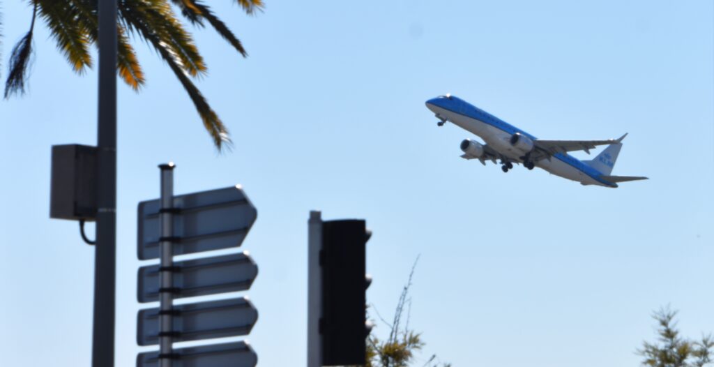 Avion de ligne au décollage aéroport Nice Côte d'Azur derrière palmier et panneaux